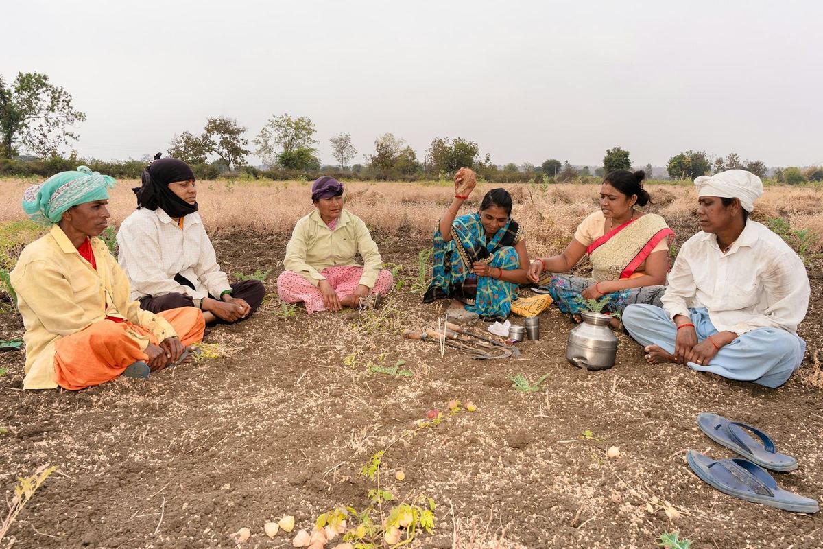 A group of villagers sit in a circle on farmland for a meeting
