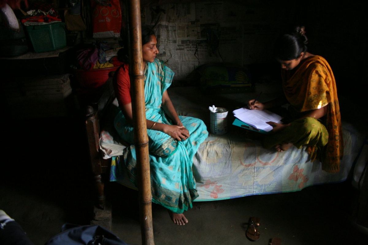 A surveyor interviews a woman in her home, recording answers on a paper form